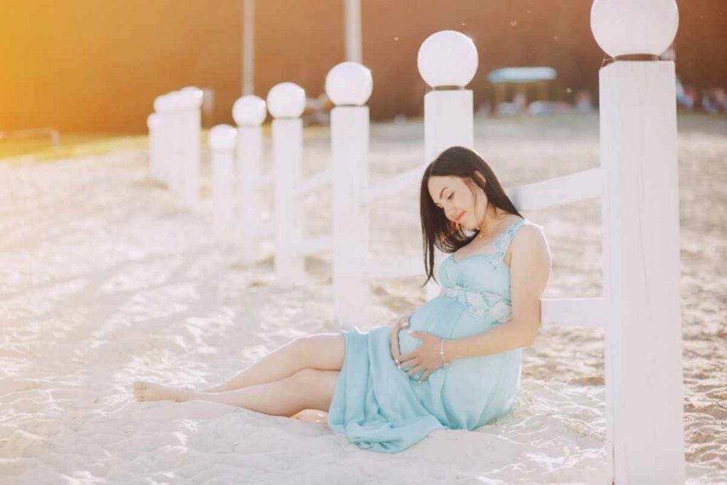 A serene beach maternity photo of a glowing mother-to-be, standing by the shore, with soft waves and golden light highlighting her baby bump in a peaceful, intimate moment.