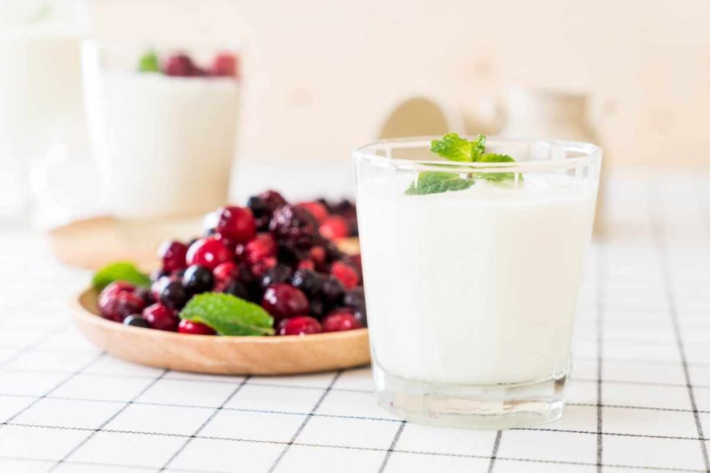 A refreshing cold yogurt drink served in a glass, garnished with fruit slices and a sprinkle of spices, offering a creamy and tangy taste.