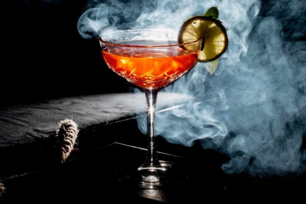 "Smoked Old Fashioned cocktail with orange peel garnish and smoke swirling in a glass"